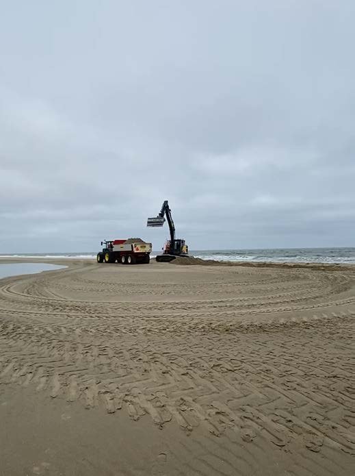 An excavator on the shore, tracks drawn across the wet sand.